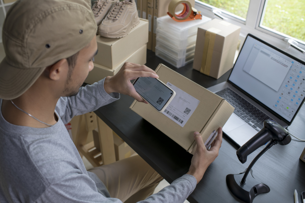 Image of an employee at a small business using a custom web app on a smartphone to scan a parcel package that is ready for shipping. 